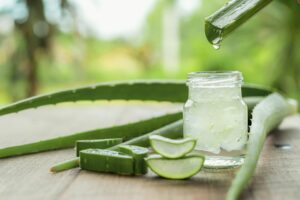 Ein Glas mit Aloe-Vera-Saft steht gemeinsam mit Aloe-Vera-Zweigen auf einem Holztisch.